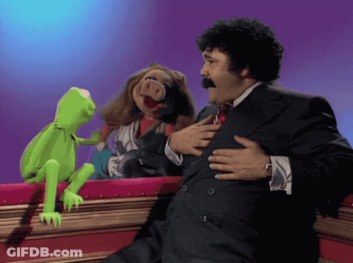 A Man In A Suit And Tie Holds His Chest While Two Muppets Look On GIF