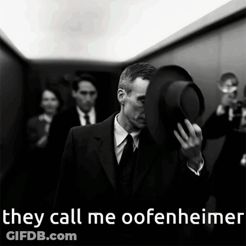 A Man In A Suit And Tie Holds His Hat Over His Face With The Words They Call Me Oofenheimer Below Him GIF