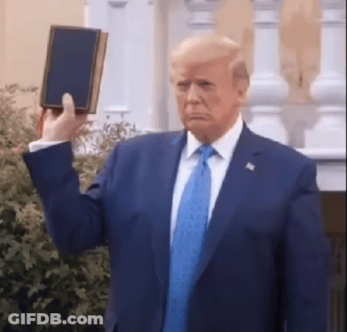 A Man In A Suit And Tie Holds Up A Bible GIF