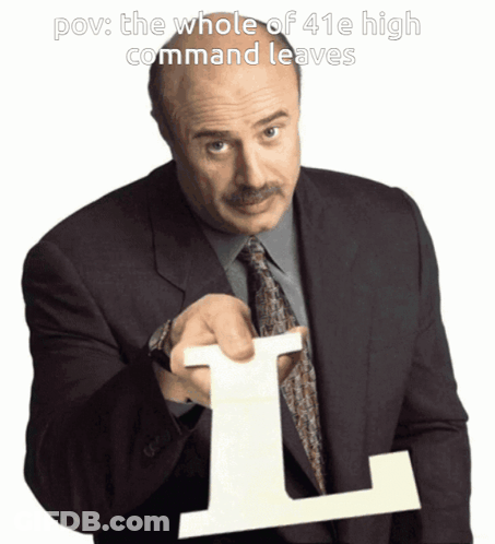 A Man In A Suit And Tie Holds Up A Large L GIF