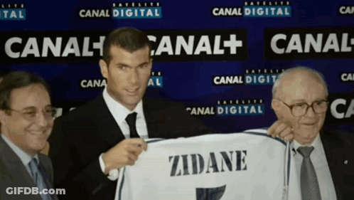 A Man In A Suit And Tie Holds Up A Zidane Shirt GIF
