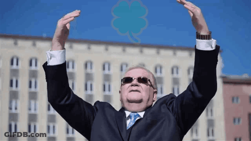 A Man In A Suit And Tie Holds Up His Arms In The Air GIF