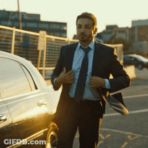A Man In A Suit And Tie Is Adjusting His Jacket GIF