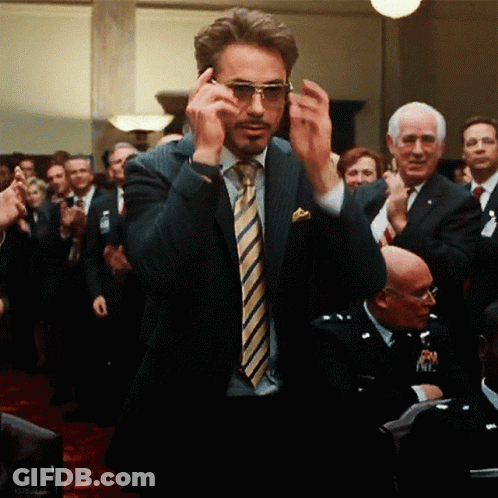 A Man In A Suit And Tie Is Adjusting His Sunglasses In Front Of A Crowd GIF