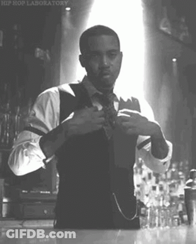 A Man In A Suit And Tie Is Adjusting His Tie In A Black And White Photo . GIF