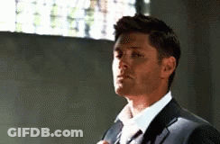 A Man In A Suit And Tie Is Adjusting His Tie In A Room . GIF