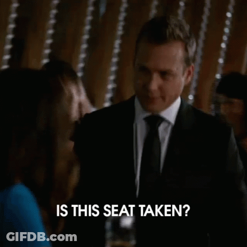 A Man In A Suit And Tie Is Asking Is This Seat Taken GIF