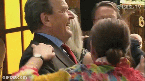 A Man In A Suit And Tie Is Being Hugged By A Woman In A Floral Shirt . GIF