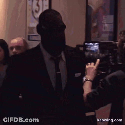 A Man In A Suit And Tie Is Being Photographed By A Woman With The Website Kapwing.com Visible GIF