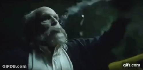 A Man In A Suit And Tie Is Blowing A Cloud Of Smoke Out Of His Mouth . GIF