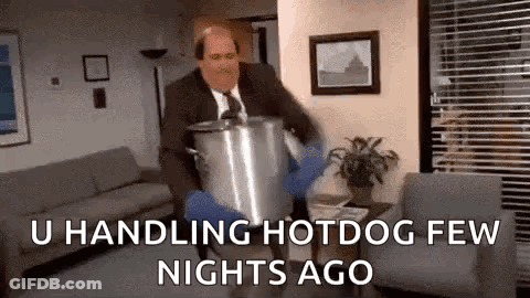 A Man In A Suit And Tie Is Carrying A Large Pot In A Living Room . GIF