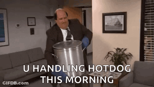 A Man In A Suit And Tie Is Carrying A Large Pot Of Hotdog In A Living Room . GIF