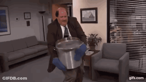 A Man In A Suit And Tie Is Carrying A Large Pot Of Water . GIF