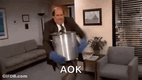 A Man In A Suit And Tie Is Carrying A Pot In A Living Room . GIF
