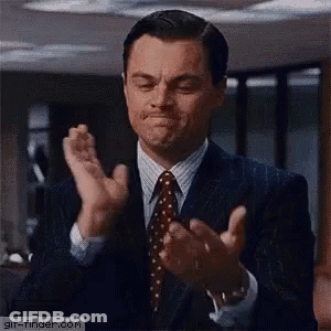 A Man In A Suit And Tie Is Clapping His Hands And Making A Face . GIF