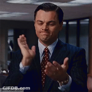 A Man In A Suit And Tie Is Clapping His Hands And Making A Face . GIF