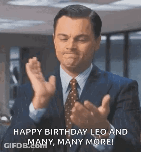 A Man In A Suit And Tie Is Clapping His Hands And Saying Happy Birthday Leo And Many , Many More . GIF