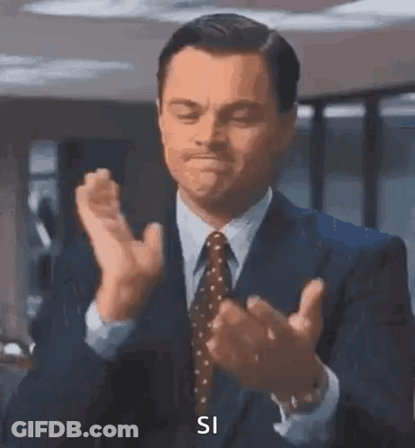 A Man In A Suit And Tie Is Clapping His Hands And Saying `` Si '' . GIF