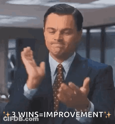 A Man In A Suit And Tie Is Clapping His Hands And Says 3 Wins = Improvement GIF