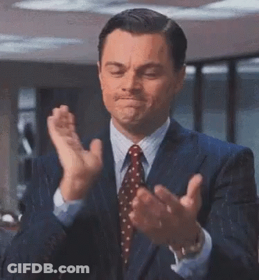 A Man In A Suit And Tie Is Clapping His Hands And Smiling . GIF