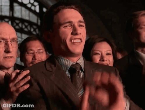A Man In A Suit And Tie Is Clapping His Hands In A Crowd GIF