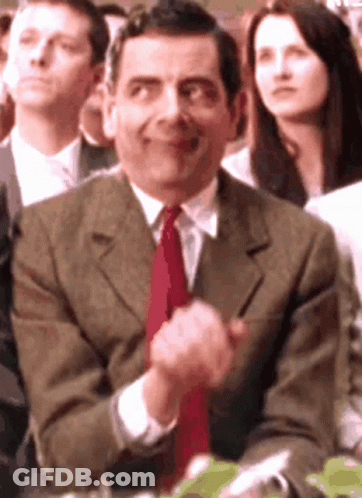 A Man In A Suit And Tie Is Clapping His Hands In A Crowd GIF