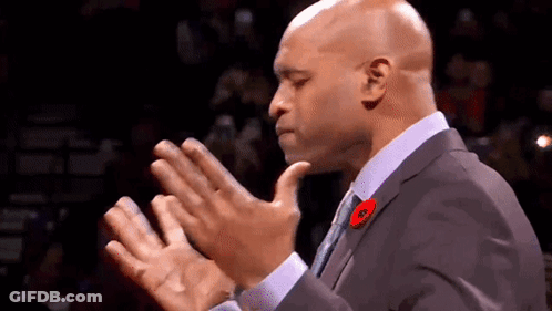 A Man In A Suit And Tie Is Clapping His Hands In A Crowd . GIF