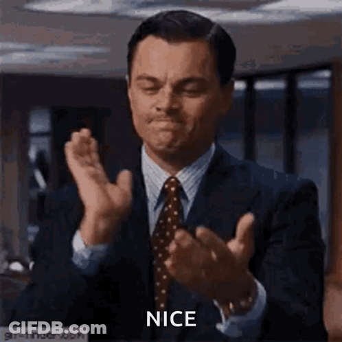 A Man In A Suit And Tie Is Clapping His Hands In A Room . GIF