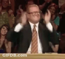 A Man In A Suit And Tie Is Clapping His Hands In Front Of A Crowd Of People . GIF