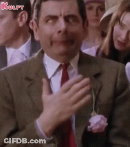 A Man In A Suit And Tie Is Clapping His Hands In Front Of A Crowd Of People . GIF