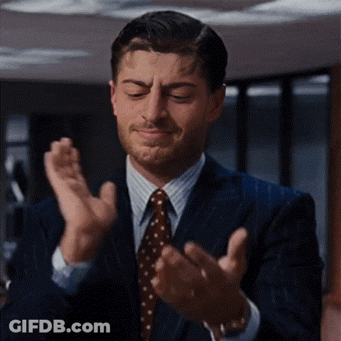 A Man In A Suit And Tie Is Clapping His Hands Together . GIF