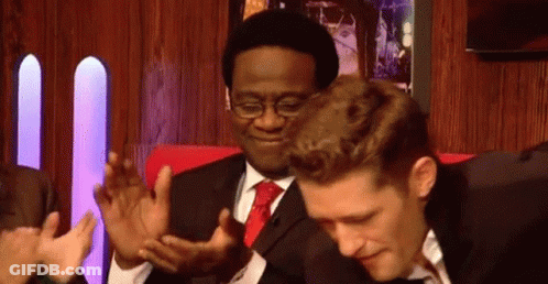 A Man In A Suit And Tie Is Clapping His Hands While Another Man Looks On . GIF