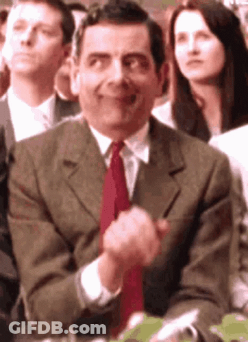 A Man In A Suit And Tie Is Clapping His Hands While Sitting In A Crowd . GIF
