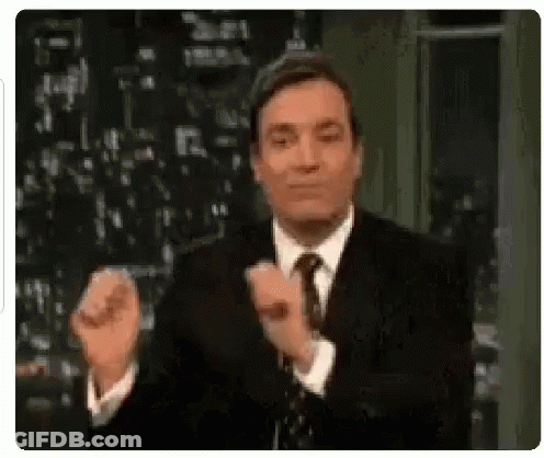 A Man In A Suit And Tie Is Clapping His Hands While Standing On A Stage . GIF