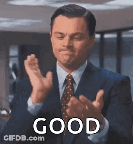 A Man In A Suit And Tie Is Clapping His Hands With The Word Good Written Below Him . GIF