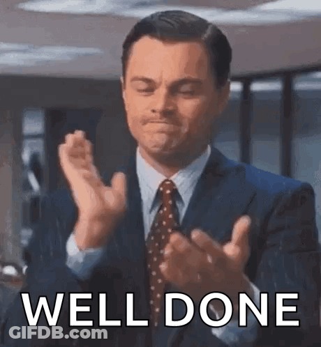 A Man In A Suit And Tie Is Clapping His Hands With The Words `` Well Done '' Behind Him . GIF