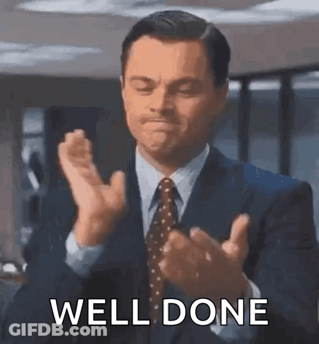 A Man In A Suit And Tie Is Clapping His Hands With The Words `` Well Done '' Written Below Him . GIF