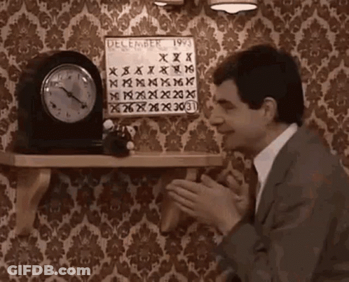 A Man In A Suit And Tie Is Clapping In Front Of A Clock And A Calendar On A Shelf . GIF