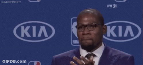 A Man In A Suit And Tie Is Clapping In Front Of A Kia Sign . GIF
