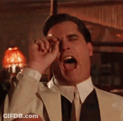A Man In A Suit And Tie Is Covering His Eyes With His Hand . GIF