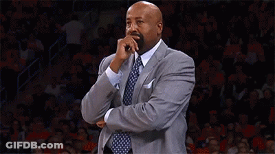 A Man In A Suit And Tie Is Covering His Mouth With His Hand While Standing On A Basketball Court . GIF