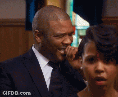 A Man In A Suit And Tie Is Crying At A Funeral While A Woman Looks On . GIF