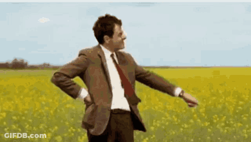 A Man In A Suit And Tie Is Dancing In A Field Of Flowers . GIF