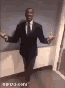 A Man In A Suit And Tie Is Dancing In A Hallway . GIF