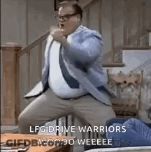 A Man In A Suit And Tie Is Dancing In A Living Room With A Table In The Background . GIF