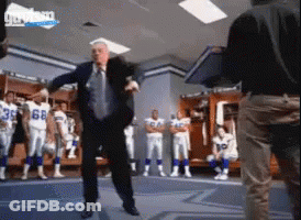 A Man In A Suit And Tie Is Dancing In A Locker Room With Football Players In The Background GIF