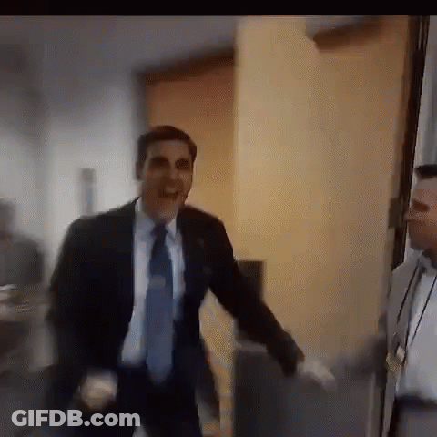 A Man In A Suit And Tie Is Dancing In A Room While Another Man Watches . GIF