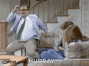 A Man In A Suit And Tie Is Dancing In Front Of A Group Of People On A Couch . GIF