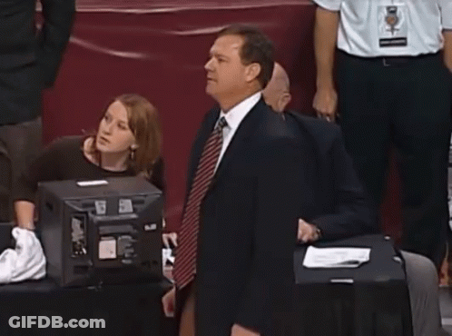 A Man In A Suit And Tie Is Dancing In Front Of A Group Of People GIF
