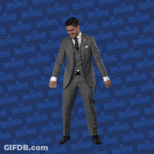 A Man In A Suit And Tie Is Dancing In Front Of A Nflers Sign GIF